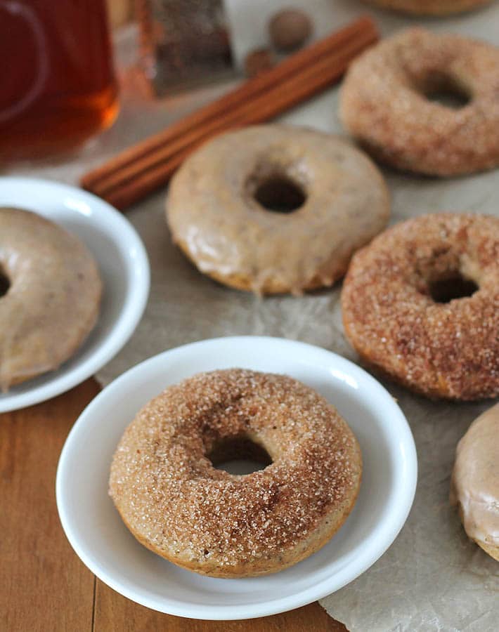 Chai-Spiced Baked Vegan Doughnuts on a table, two doughnuts are on small white plates.