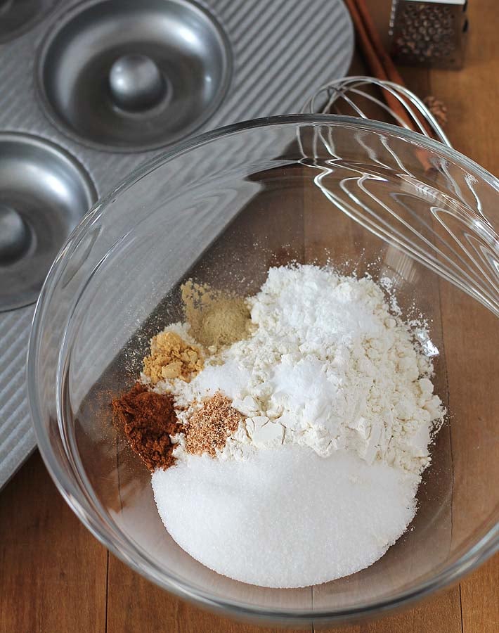 Overhead shot of the dry ingredients for Chai-Spiced Baked Vegan Doughnuts in a glass bowl, bowl is sitting on a wood table.