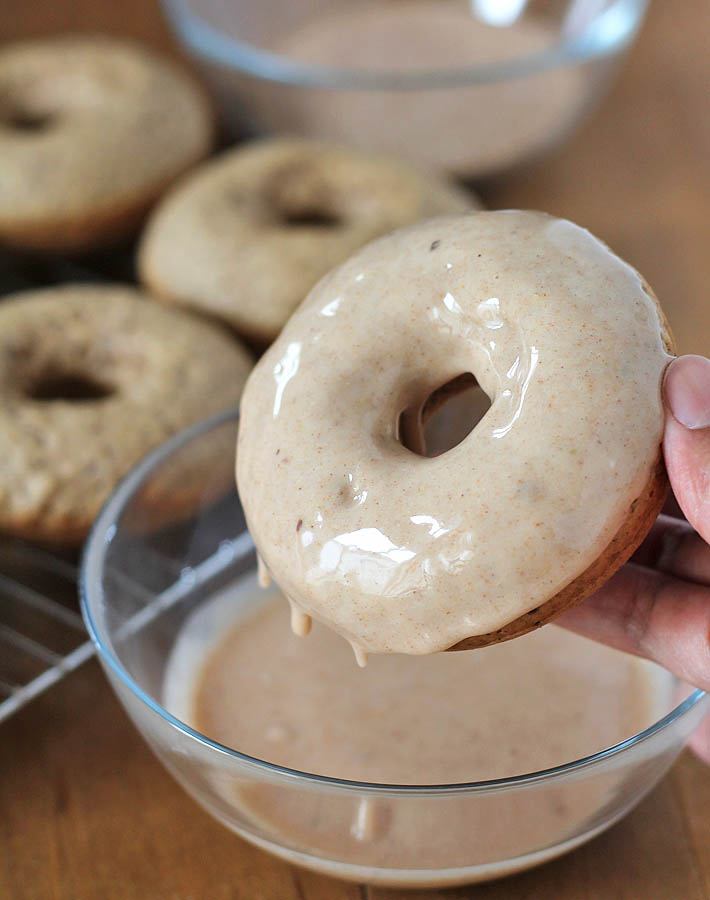 Chai-Spiced Baked Vegan Doughnuts being dipped in chai flavoured sugar glaze.
