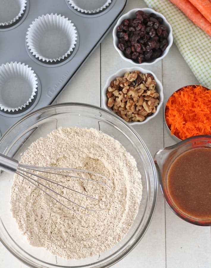 Overhead shot of the ingredients for vegan carrot muffins sitting on a white wooden table.