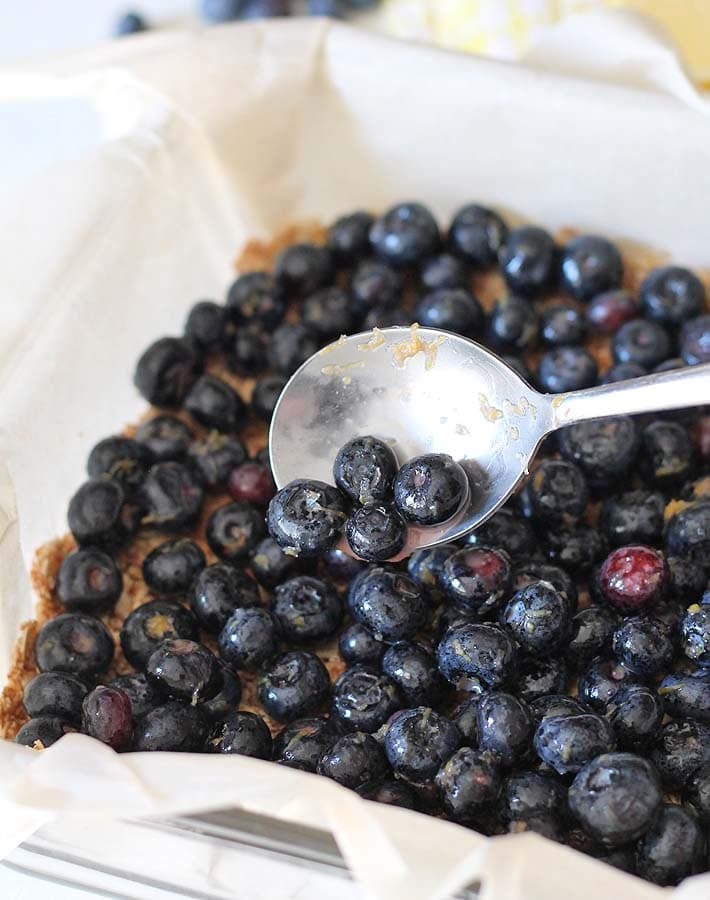 Fresh blueberries being spooned on top of the crust to make Blueberry Oatmeal Bars.