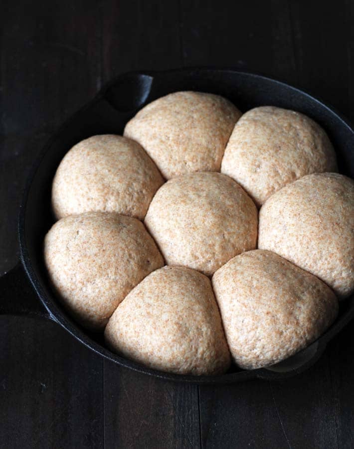 Dough for spelt rolls after rising for a second time in a cast iron pan sitting on a black wood table.