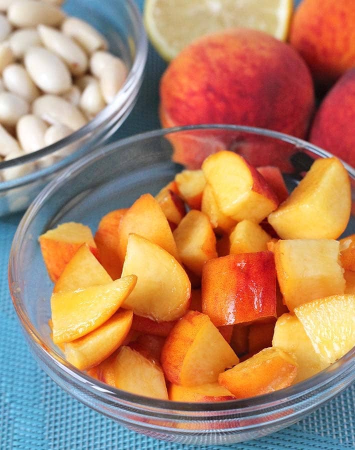 Some of the ingredients for No Bake Peach Cheesecake bites on a table (fresh peaches, almonds, lemon)