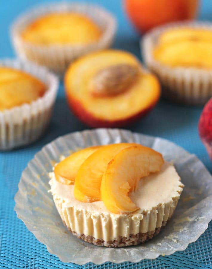 No Bake Peach Cheesecake bites on a blue placemat with fresh peaches around them.