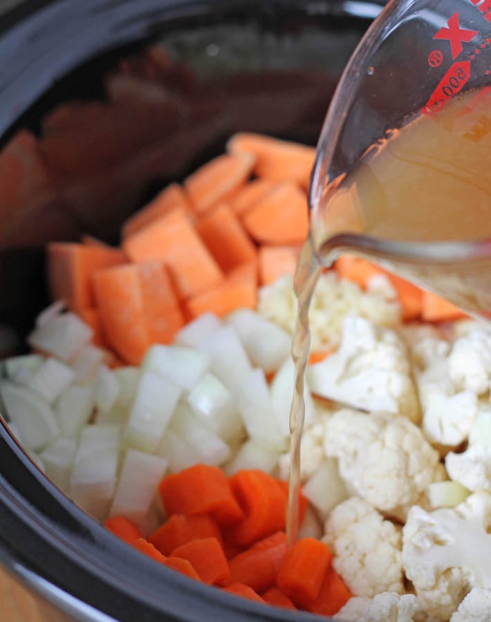 Broth being poured over vegetables in slow cooker for Cauliflower Sweet Potato Soup.