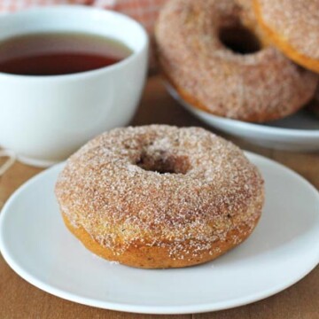 Vegan Baked Pumpkin Doughnuts on white plates on a wood table.