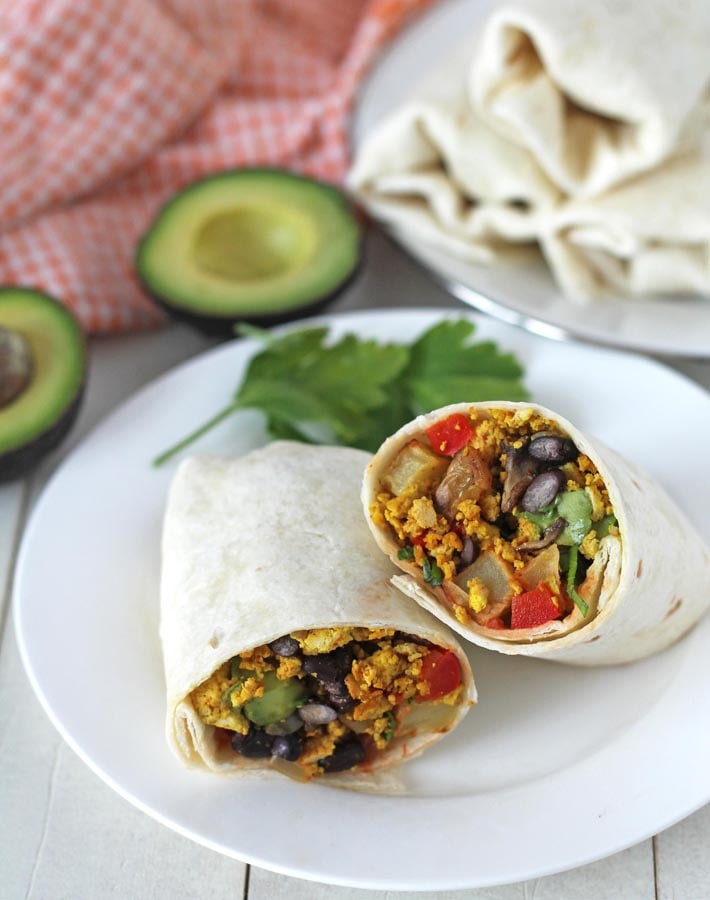 Tofu Breakfast Burritos on white plates, the burrito in the front is cut in half so the inside is visible.