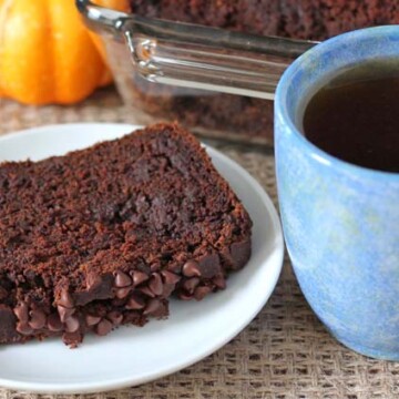 A slice of Chocolate Pumpkin Bread on a white plate with a blue mug filled with tea to the right.