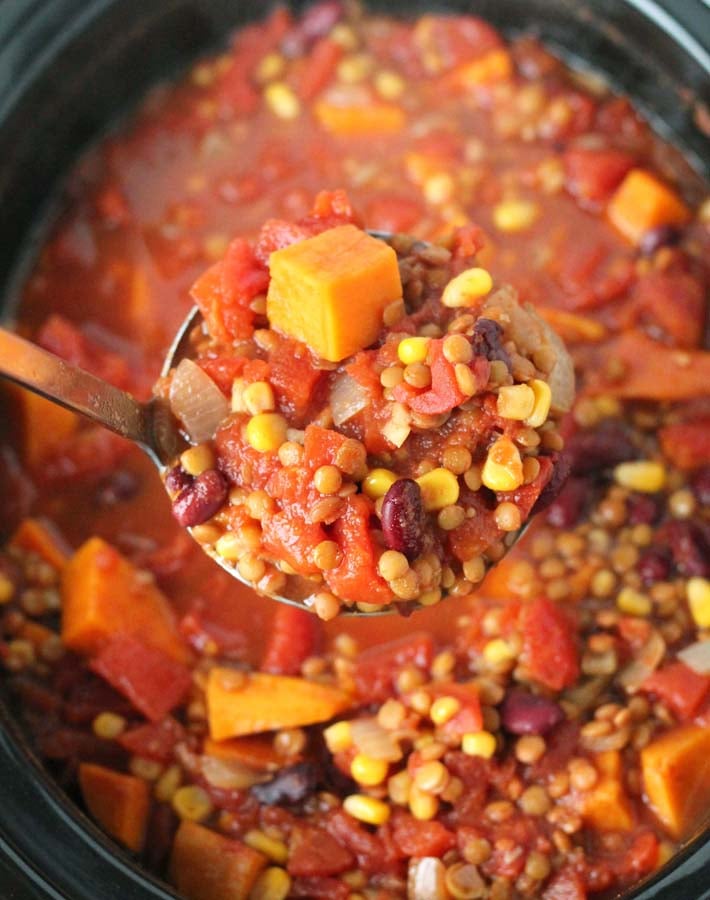 An up close shot of a ladle full of Lentil Sweet Potato Chili over the slow cooker it came from.