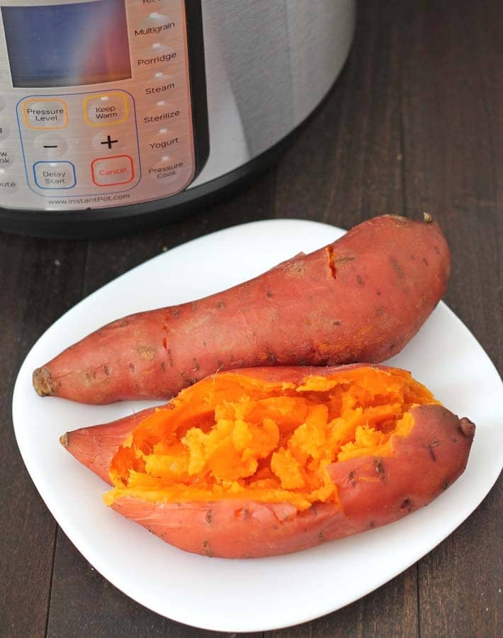 Two Instant Pot Sweet Potatoes on a white plate, one potatoe has been split open to show the inside.