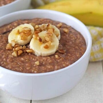 Banana Steel Cut Oats in a bowl on a white table with a spoon to the left of the bowl.