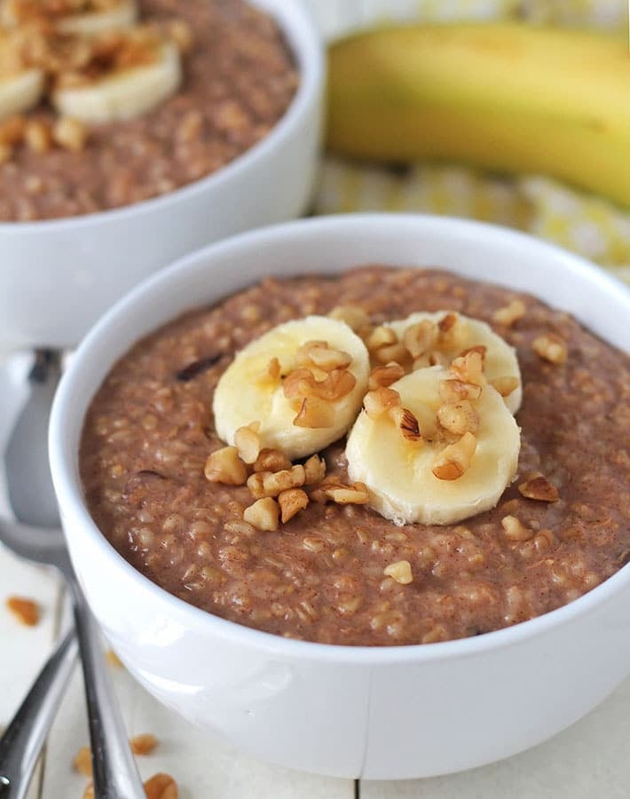 Two bowls of Banana Steel Cut Oats in white bowls on a white table.