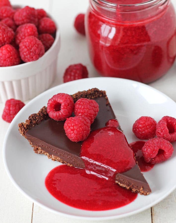 A slice of chocolate truffle tart with easy raspberry sauce drizzled on top of it.