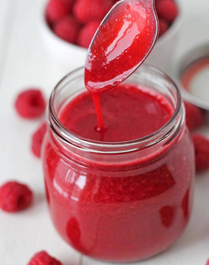 Easy Raspberry Sauce being drizzled off a spoon in a mason jar full of the sauce.