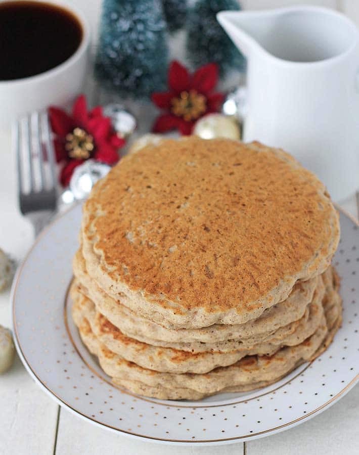 Four gluten free vegan pancakes on a holiday plate, a cup of coffee and Christmas decorations sit behind.