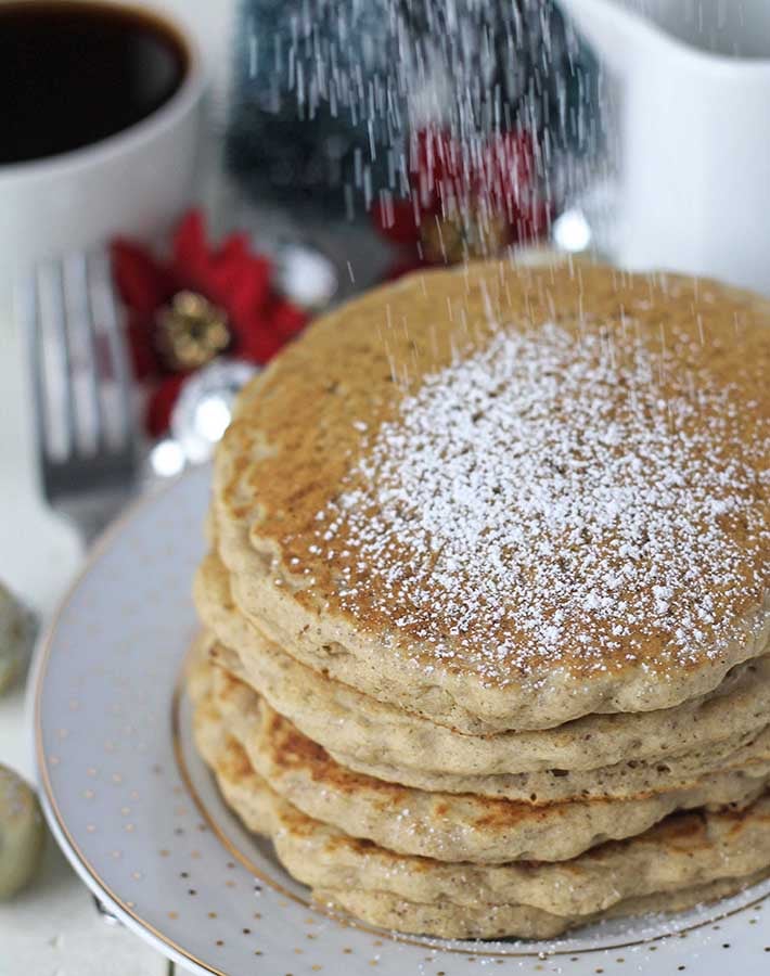 Powdered sugar being sifted on top of a plate of eggnog pancakes.