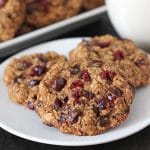 Three Oatmeal Cranberry Chocolate Chip Cookies on a plate, glass of almond milk sits in the background.