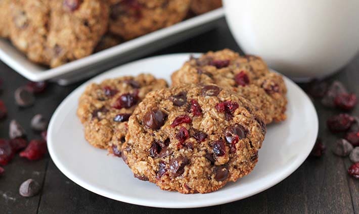 Three Oatmeal Cranberry Chocolate Chip Cookies on a plate, glass of almond milk sits in the background.