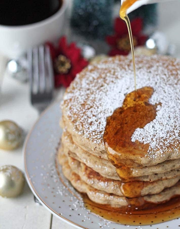 Maple syrup being poured onto a stack of gluten free vegan eggnog pancakes.