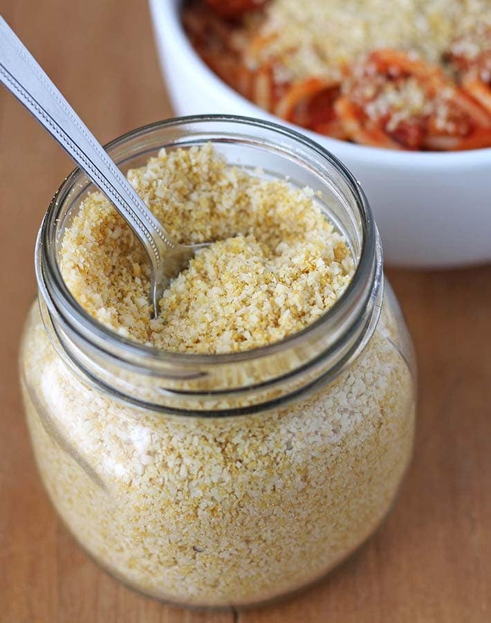 A spoon in a glass jar of vegan parmesan.