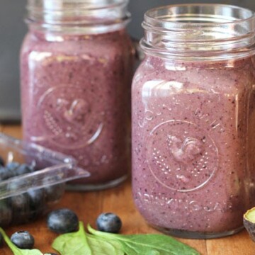 Blueberry Pineapple Smoothie in two mason jar glasses on w brown wooden table.