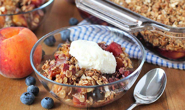 Vegan Peach Blueberry Crisp in a bowl topped with a small scoop of ice cream.