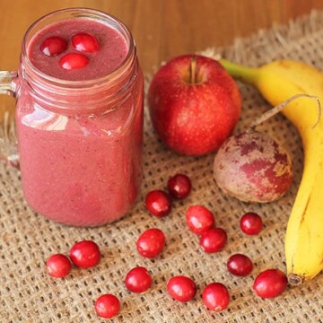Cranberry Apple Smoothie in a mason jar mug on a burlap placemat with smoothie ingredients to the right.