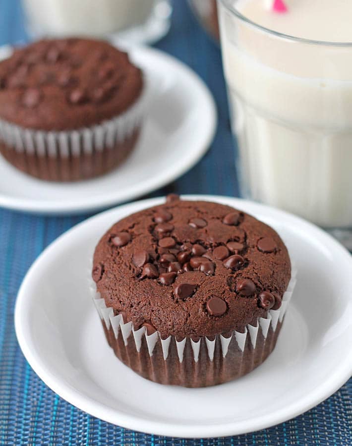 Gluten-Free Vegan Chocolate Muffins on a blue placemat, muffins are sitting on individual small plates.