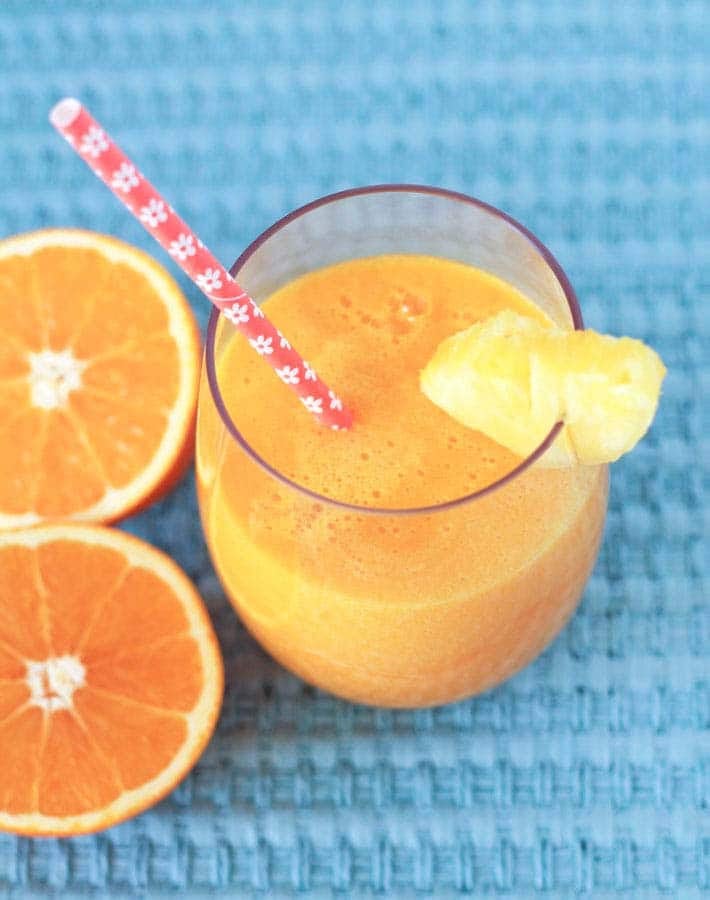 Overhead shot of a glass of Pineapple Orange Mango Juice with a straw in the glass.