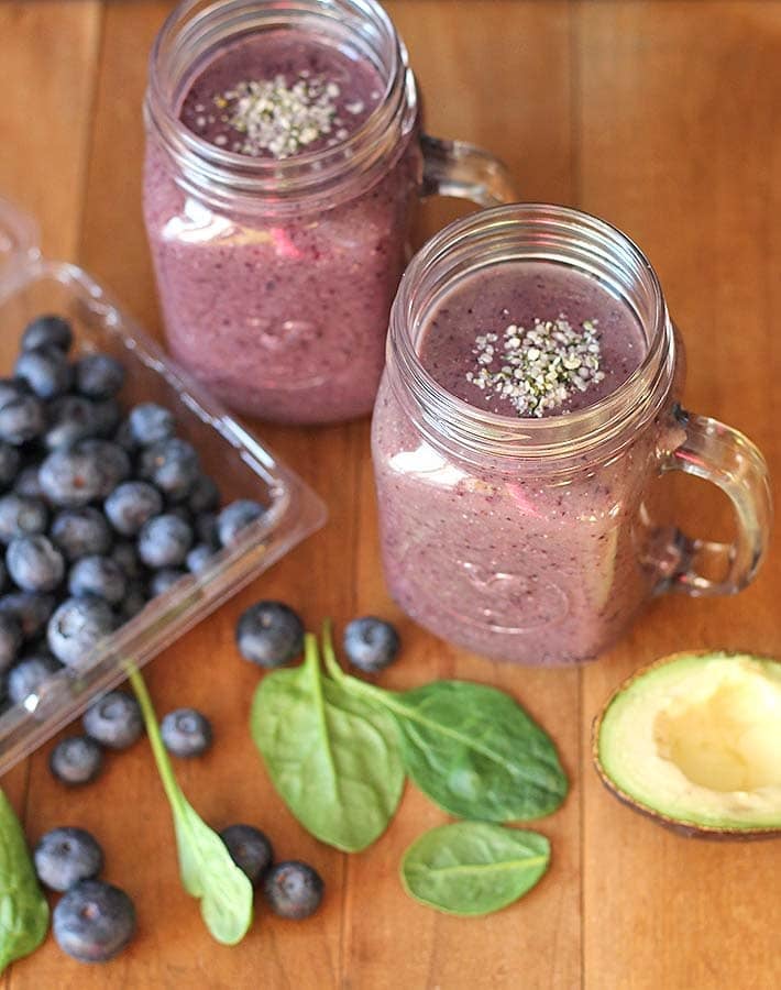 Overhead shot of two blueberry pineapple smoothie glasses on a brown table.