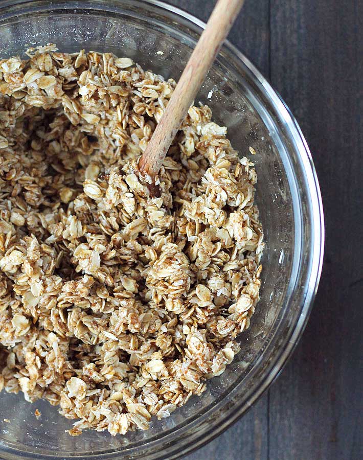 Mixture for nut free granola in a glass bowl with a wooden spoon.