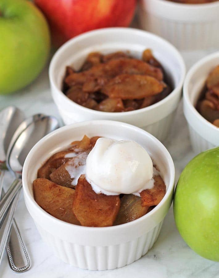 A remekin with baked cinnamon apple slices topped with a small scoop of coconut ice cream.