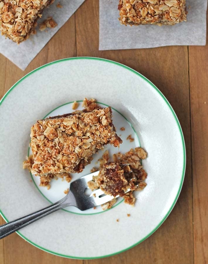 Overhead shot of a vegan date square on a white plate, a piece of the square is on a fork.