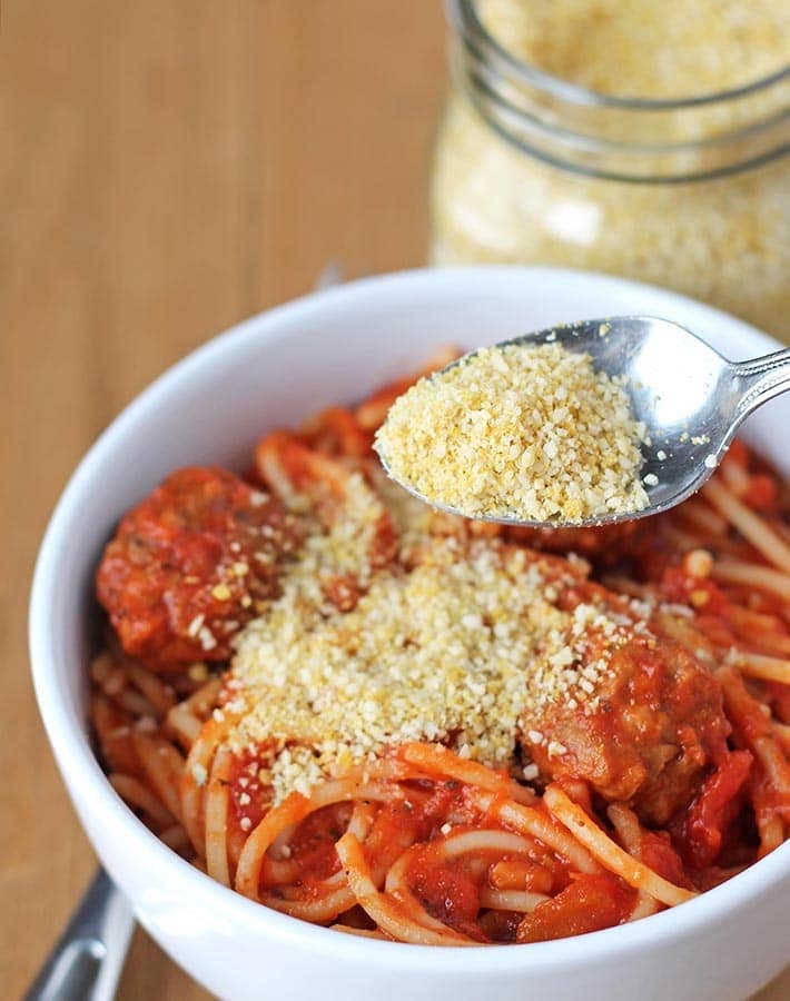 Vegan parmesan being sprinkled from a spoon onto a bowl of spaghetti.