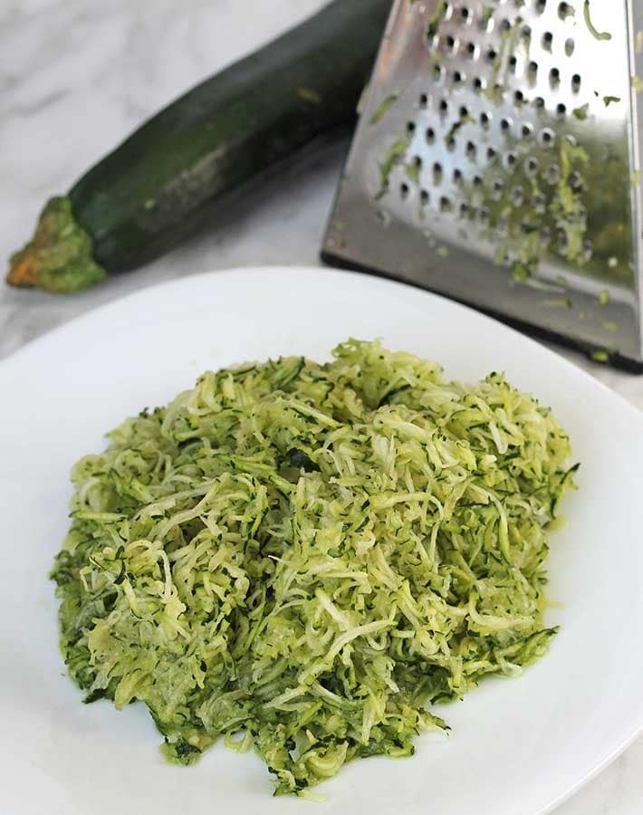 Shredded zucchini on a white plate to be used to make Gluten-Free Banana Zucchini Bread.