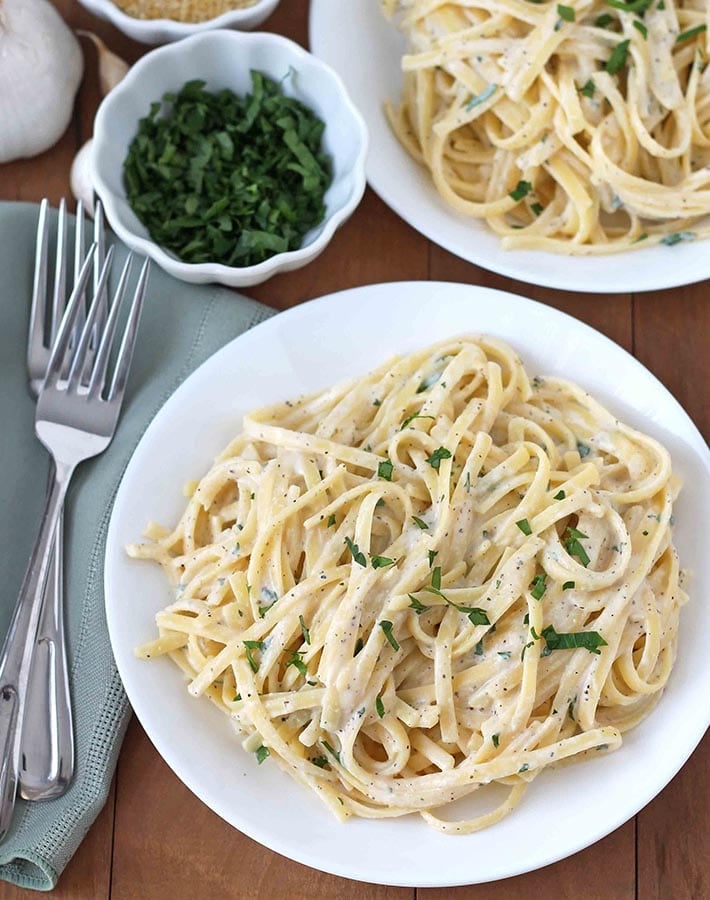 Overhead shot of Vegan Garlic Pasta Sauce on two white plates, plates are sitting on a brown wooden table.