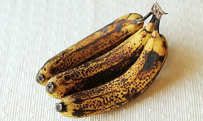 A bunch of overripe bananas sitting on a cream coloured placemat.