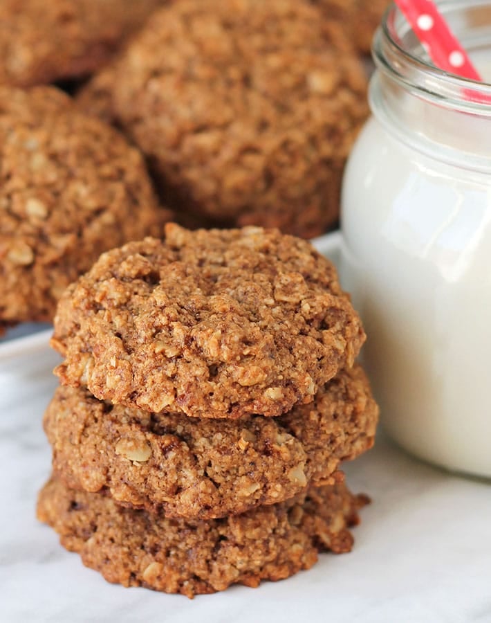 A stack of three Vegan Gluten Free Oatmeal Cookies sitting on a marble surface, a glass of milk sits to the right.