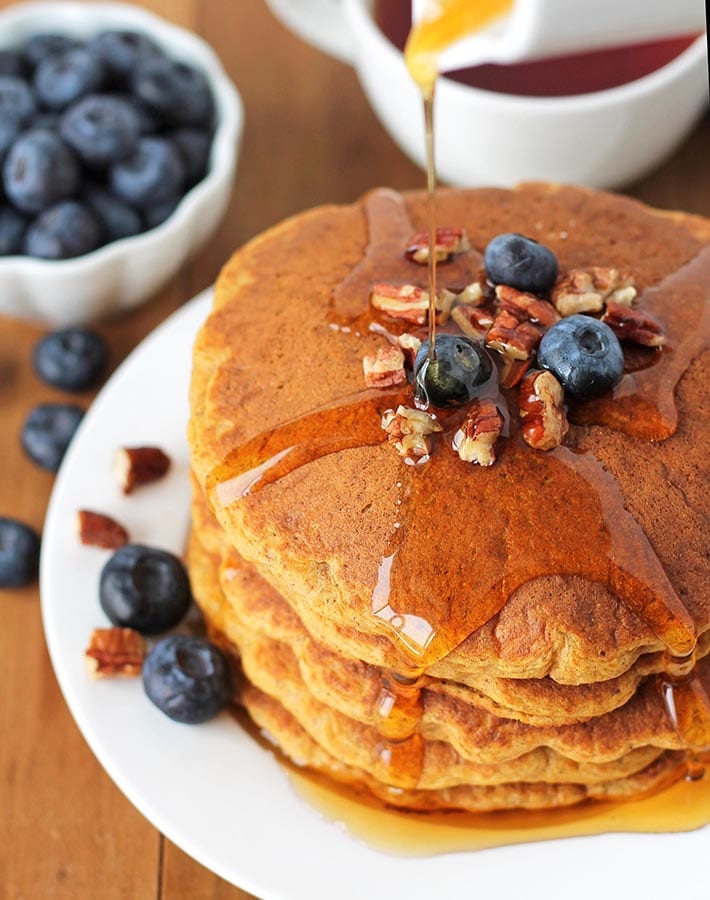 A stack of Gluten Free Sweet Potato Pancakes on a plate with syrup being poured on top.