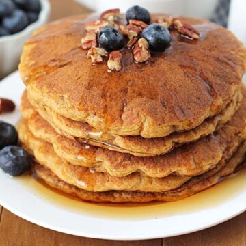 Four Gluten Free Sweet Potato Pancakes on a white plate garnished with fresh blueberries and pecans.