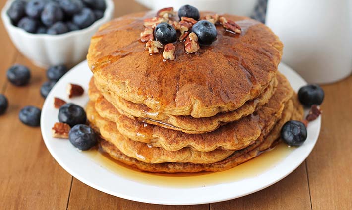 Four Gluten Free Sweet Potato Pancakes on a white plate garnished with fresh blueberries and pecans.