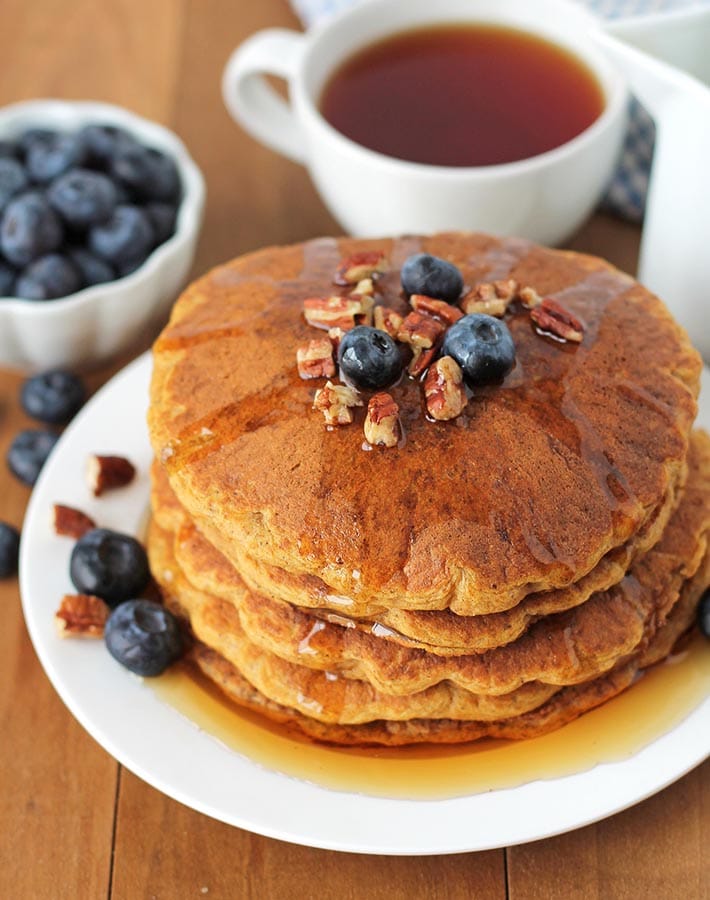 Gluten Free Sweet Potato Pancakes on a white plate with syrup, fresh blueberries and pecans on top.