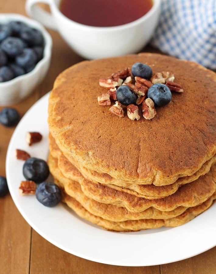 A stack on four Gluten Free Sweet Potato Pancakes on a white plate with blueberries and pecans on top.