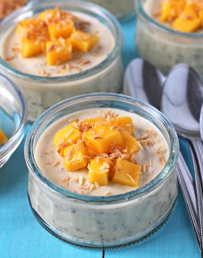 Small jars of Coconut Mango Chia Pudding on a blue table.