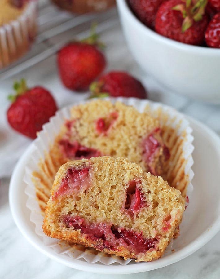 A vegan strawberry muffin cut in half on a small white plate.
