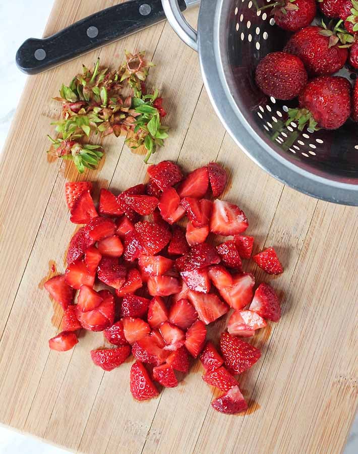 Chopped strawberries on a bamboo cutting board.