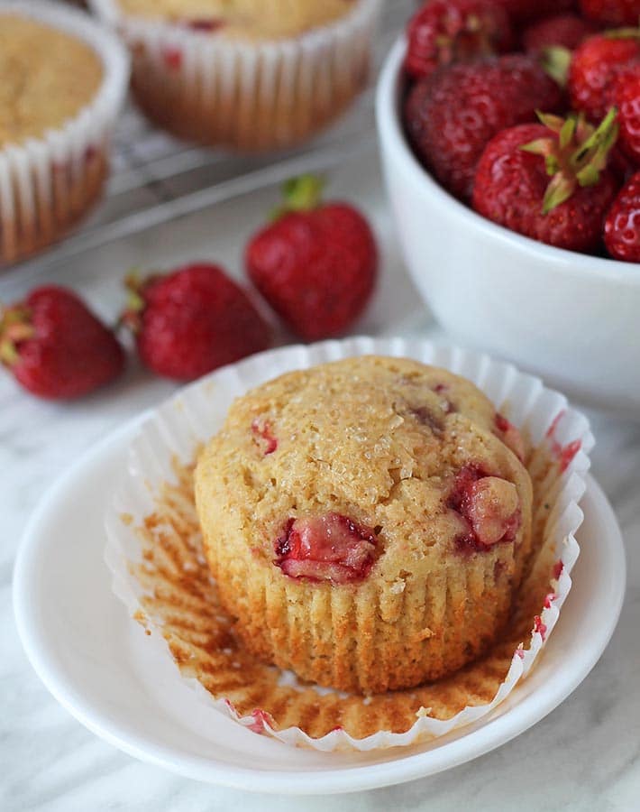 Gluten free strawberry muffin on a small white plate with the muffin wrapper peeled off.