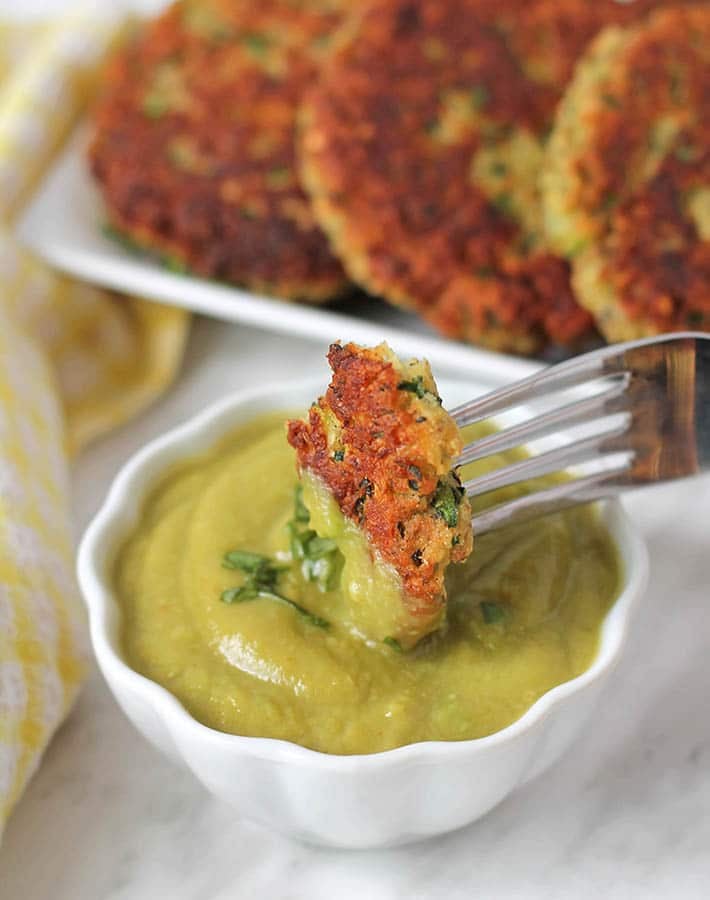 A piece of a gluten free vegan zucchini fritter being dipped into avocado crema.