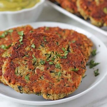 Three fried zucchini fritters ona plate, fritters are garnished with chopped parsley.