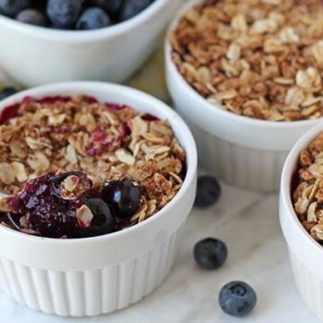 Three bowls of blueberry crisp with oatmeal on a marble surface.